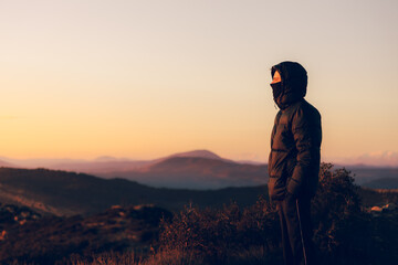 young traveler wrapped up on top of a mountain watching the sunset with some nice mountains in the background