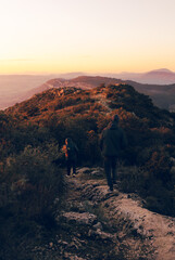 Couple walking on top of the mountain on a stone path watching a beautiful sunset with orange and pink sky