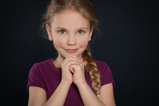 Girl with clasped hands praying on black background