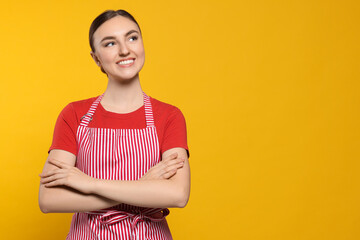 Beautiful young woman in clean striped apron on orange background. Space for text