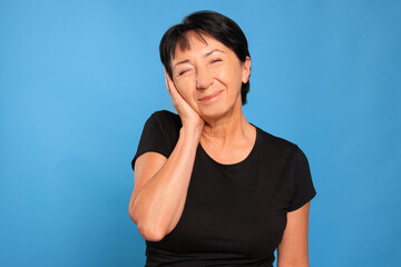 Senior woman suffering from ear pain on light blue background