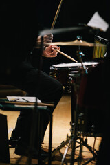 A seated drummer plays drums on a theater stage during a concert