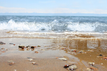Defocused beach with blurred wave and wet sand with pebble on blue sky. Sea, ocean background. Vacation outdoor and travel holiday adventure concept