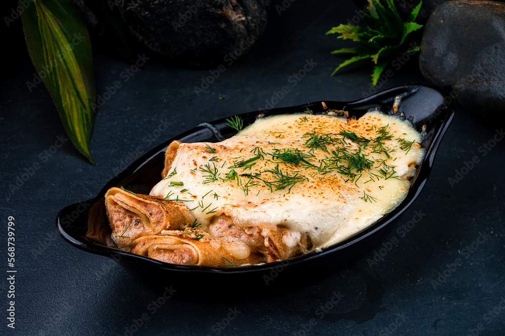 Sticker Thin pancakes with ham and cheese sauce in a cast-iron bowl.