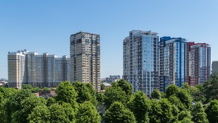Fototapeta na wymiar View from window on multi-storey multi-apartment residential complexes. High-rise residential buildings against blue spring sky. Park areas for recreation and walks. Krasnodar, Russia - May 26, 2022