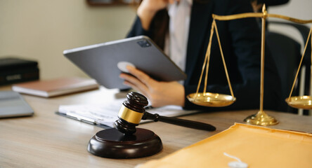 Male lawyer in the office with brass scale and using tablet and laptop on wooden table. justice and...