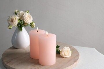 Burning candles and beautiful roses on white table, space for text