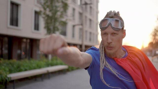 Portrait of comic funny crazy young businessman in suit wearing superman outdoors. Leader success winner superhero crazy man with red cape running on city street, business. People and work concept.