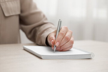 Fototapeta premium Woman writing in notebook at wooden table, closeup