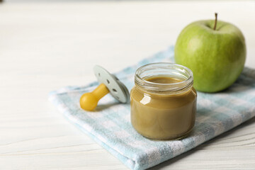 Jar with healthy baby food, apple and pacifier on white wooden table. Space for text