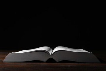 Open Bible on wooden table against black background. Christian religious book
