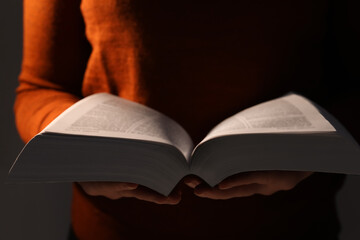 Woman reading Bible against black background, closeup