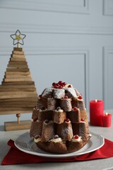 Delicious Pandoro Christmas tree cake with powdered sugar and berries near festive decor on white marble table