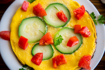 Fried omelet with zucchini, tomatoes, herbs in a plate