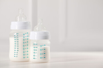 Feeding bottles with milk on white wooden table. Space for text