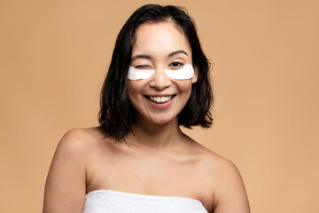 Smiling asian woman with eye patches winking isolated on beige
