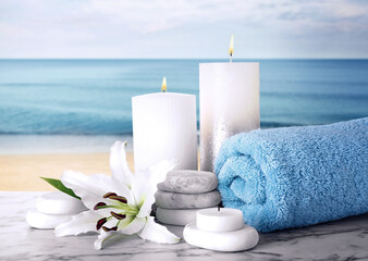 Obraz na płótnie Canvas Composition with towel, spa stones and candles on marble table against seascape
