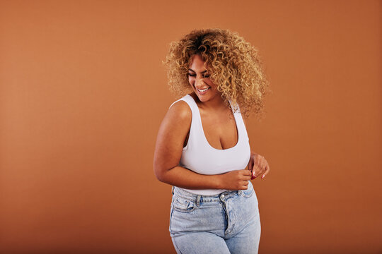 Laughing young woman in jeans standing against an orange background