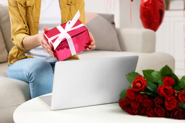 Valentine's day celebration in long distance relationship. Woman holding gift box while having video chat with her boyfriend via laptop indoors, closeup