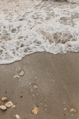 Closeup seascape image of foam and small sea waves with clear water on sandy textured beach with small stones in daily light. Travel, tourism and adventures. Summer holidays on coastline