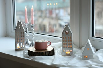 Beautiful house shaped candle holders and hot dink with marshmallow on windowsill indoors