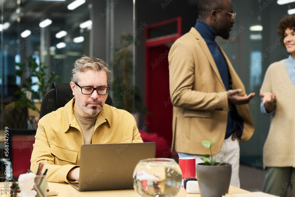 Aufkleber serious mature businessman networking in front of laptop while sitting by desk against two young int