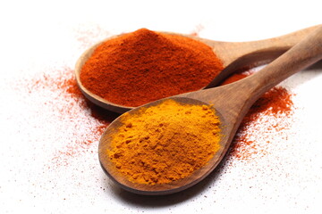 Turmeric powder pile and red paprika, cayenne pepper in wooden spoon isolated on white  