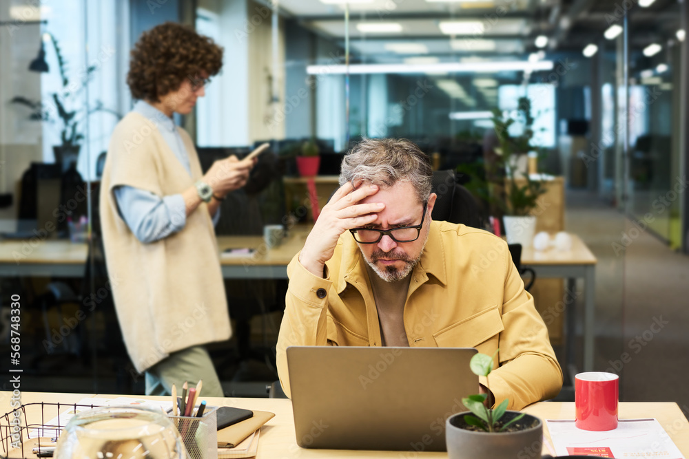 Poster Mature chief executive officer frowning and expressing misunderstanding while trying to understand data on laptop screen during network