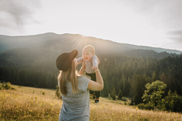 Mother throws up his happy son into sky with his hands. Walking in nature on an autumn day. Mom and baby child playing in the mountains. Family spending time together on vacation. World Tourism Day.