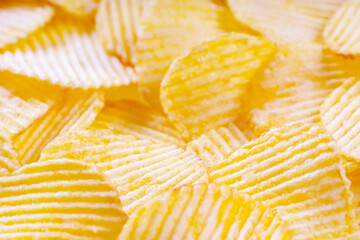 Yellow crispy ridged potato chips close up. Food background, banner, header, wallpaper.