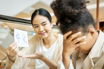 Discouraged African woman learning Chinese language with her female teacher, holding Chinese...