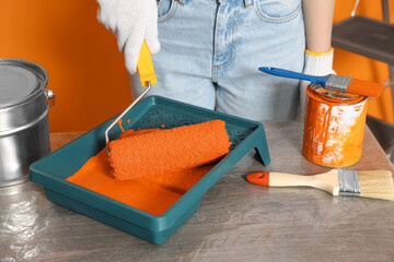 Woman taking orange paint with roller from tray at table, closeup