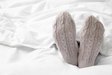 Woman in warm socks lying on bed, closeup. Space for text