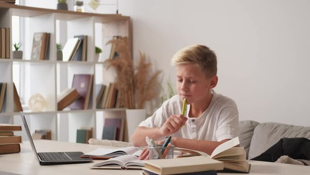 Homework inspiration. Casual boy. Home education. Smiling teenager kid studying writing copybook sitting desk light room interior.