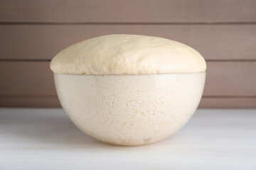Bowl of fresh yeast dough on white wooden table