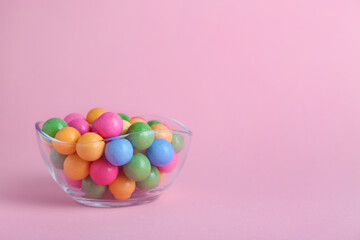 Fototapeta na wymiar Bowl with many bright gumballs on pink background. Space for text