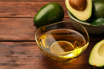 Cooking oil in bowl and fresh avocados on wooden table, closeup