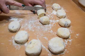 closeup of female hands in flour with a knife cut dough sausage in small pieces
