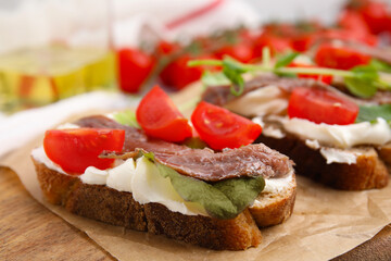 Delicious bruschettas with anchovies, tomatoes, microgreens and cream cheese on wooden board, closeup
