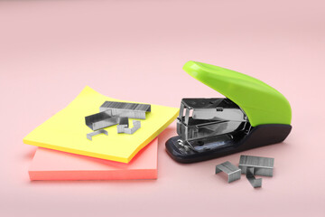 New bright stapler with staples and sticky notes on pink background. School stationery