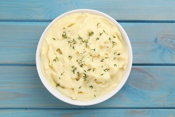 Bowl of tasty mashed potato with rosemary on light blue wooden table, top view