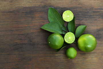 Whole and cut fresh ripe limes with green leaves on wooden table, flat lay. Space for text