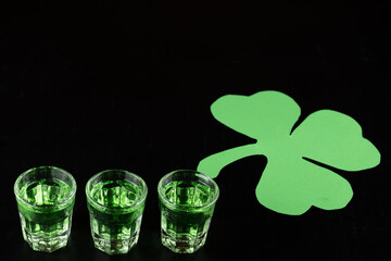 Shamrock shot glasses lined up against black background filled with emerald green spirit cocktail to be drunk at celebrations for St Patrick's day. Irish holiday is drinking event when people party
