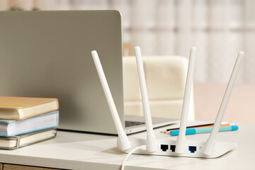 New Wi-Fi router near laptop on white table indoors