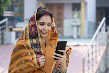 Indian rural woman in traditional saree and using smartphone at home.