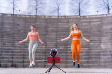 Two young fitness girls in a city park, recording the class with the phone for the followers of social networks