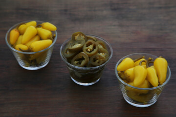 Pickled green and yellow jalapeno peppers on wooden table