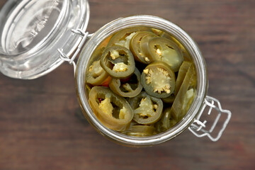 Glass jar of pickled green jalapeno peppers on wooden table, top view
