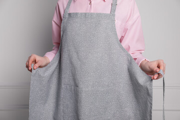 Woman putting on grey apron against white wall, closeup