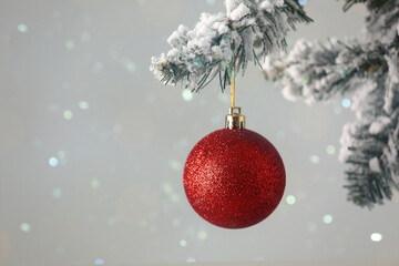 Red ball hanging on Christmas tree covered with snow against grey background. Space for text